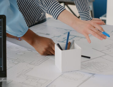 Close up of architects doing teamwork to design blueprints plans for building model on table. Team of women working with industrial sketch and layout print plan. Architectural project